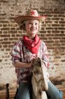 Menina jovem vestida de vaqueira com cavalo de balanço — Fotografia de Stock