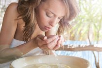 Jovem mulher com as mãos de xícara rosto de limpeza sobre tigela no spa — Fotografia de Stock