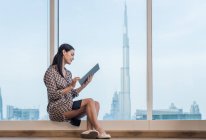 Businesswoman using digital tablet sitting at window, Dubai, United Arab Emirates — Stock Photo
