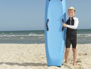 Portrait of boy nipper (child surf life savers) next to surfboard, Altona, Melbourne, Australia — Stock Photo