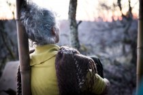 Visão traseira da mulher madura sentada no alpendre da floresta assistindo ao pôr do sol — Fotografia de Stock