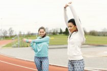 Dos mujeres jóvenes en pista de atletismo, ejercicio, estiramiento - foto de stock