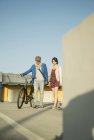 Jovem casal empurrando bicicleta ao longo da rua — Fotografia de Stock