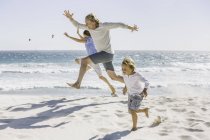Father and children jumping on beach — Stock Photo