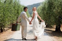 Newlyweds walking on country road with suitcase — Stock Photo