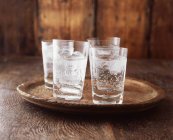 Sparkling water in drinking glasses with ice on vintage wooden plate — Stock Photo