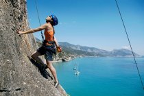 Woman rock climbing, bay in background — Stock Photo