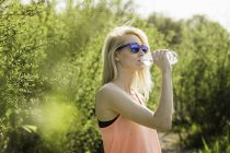 Молода жінка в парку п'є пляшку води — стокове фото