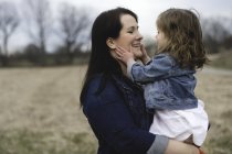Mother holding young daughter, outdoors, face to face, smiling — Stock Photo