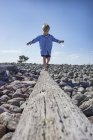 Boy balancing on log on beach — Stock Photo