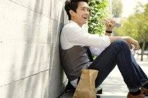 Молодий чоловік сидить на тротуарі, сміючись — стокове фото