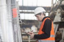 Young male warehouse worker stock taking with clipboard in warehouse — Stock Photo