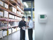 Office manager and worker discussing energy use near thermostat in factory — Stock Photo