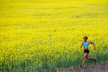Молодая женщина бежит рядом с полем рапса — стоковое фото