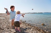 Padre e hijo tiran piedras a la playa - foto de stock
