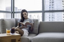 Jovem mulher no sofá livro de leitura — Fotografia de Stock
