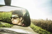Reflexão do espelho do jovem dirigindo na estrada de campo — Fotografia de Stock