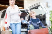 Mother with baby car seat and son carrying box of plants — Stock Photo