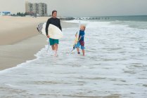 Father and son walking along beach, carrying surfboards — Stock Photo