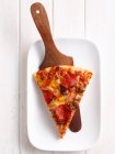 Slice of pizza on wooden spatula in platter — Stock Photo