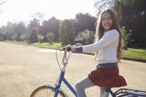 Дівчина сидить на велосипеді в парку дивиться на камеру посміхаючись — стокове фото