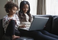 Two sisters sitting on sofa and using laptop — Stock Photo