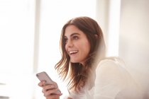 Happy young woman using smartphone in front of window — Stock Photo