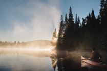 Hombre mayor navegando en canoa en el lago al amanecer - foto de stock