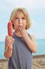 Child with fingers on lip holding ice lolly — Stock Photo