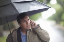 Uomo d'affari che parla al cellulare mentre trasporta ombrello — Foto stock