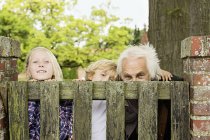 Grandfather and grandchildren peering over wooden gate — Stock Photo