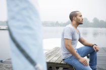 Junger Mann sitzt auf Steg — Stockfoto