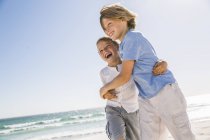 Hermanos en la playa abrazándose mirando hacia otro lado sonriendo - foto de stock