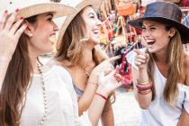 Young women trying on hats in market — Stock Photo