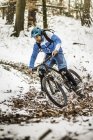 Young male mountain biker speeding on snow covered forest track — Stock Photo