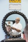 Barber shaving male client hair in salon, reflection in round mirror — Stock Photo