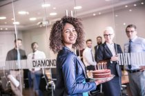 Portrait of young businesswoman carrying celebration cake into boardroom — Stock Photo