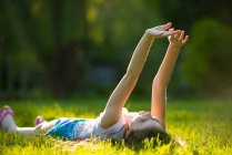Chica acostada en la hierba con los brazos levantados - foto de stock