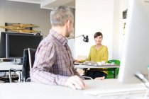 Архітектори в офісі використовують комп'ютер, розмовляють і посміхаються — стокове фото