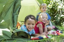 Портрет трех улыбающихся детей, лежащих в садовой палатке — стоковое фото