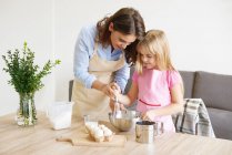 Mãe ajudando filha batem ingredientes juntos na tigela — Fotografia de Stock