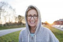 Portrait of woman wearing eyeglasses and hooded top looking at camera smiling — Stock Photo