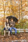 Couple sitting on fence with umbrella — Stock Photo