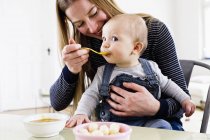 Mulher alimentando bebê filha à mesa — Fotografia de Stock