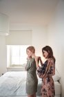 Две молодые женщины готовятся в спальне, застегивая платья — стоковое фото