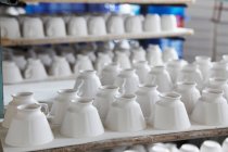 Белые чашки на столе на керамической фабрике — стоковое фото