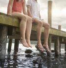 Casal jovem de mãos dadas e sentado na borda do molhe sobre o lago, cortado — Fotografia de Stock