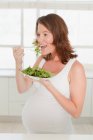 Donna incinta mangiare insalata in cucina — Foto stock