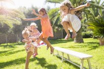 Five energetic girls jumping from garden bench — Stock Photo