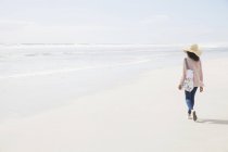 Rückansicht einer jungen Frau, die am Strand spaziert — Stockfoto